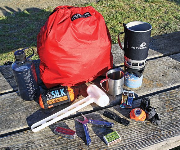Lazy camping essentials: Shatterproof Nalgene bottle for water or high-octane beverages, silk sleeping bag liner (good for another 15 degrees), stake mallet, multitool, windproof matches, LED flashlight/headlight, cup, coffee, stove. Aerostich LP grocery bag doubles as a lightweight backpack.