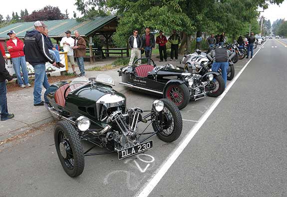 The main street in the town of Vashon is packed with vehicles for the Isle of Vashon TT, including this trio of three-wheelers; to the left is a 1938 Morgan, to the right a 2014 Morgan, and in the middle a 2007 Ace Cycle-Car.