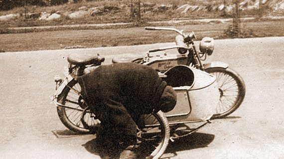 En route: an unidentified blacksmith kneels over the sidecar to inspect the connecting hardware. The heavy “bathtub” often came loose under stress, until Effie had a set of super robust springs installed.