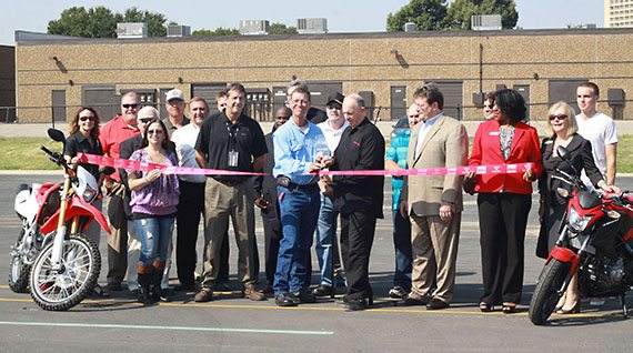 Those in attendance at the Ribbon Cutting Ceremony include: Curt Liles, Geo-Center Motorcycle Training, LLC (light-blue shirt); Gary Martini, American Honda Rider Education Manager (black shirt); Jeff King, Irving Chamber of Commerce (tan suit); Kissena Sheets, Irving Chamber of Commerce (red jacket). Also pictured are various associates of American Honda Motor Co., Geo-Center Motorcycle Training coaches, and the Irving Chamber of Commerce members.