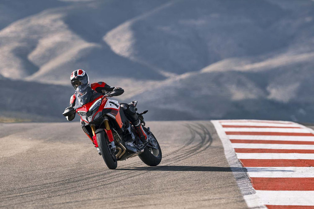 2022 Ducati Multistrada V4 Pikes Peak drives down a paved road under a mountain, next to red and white stripes