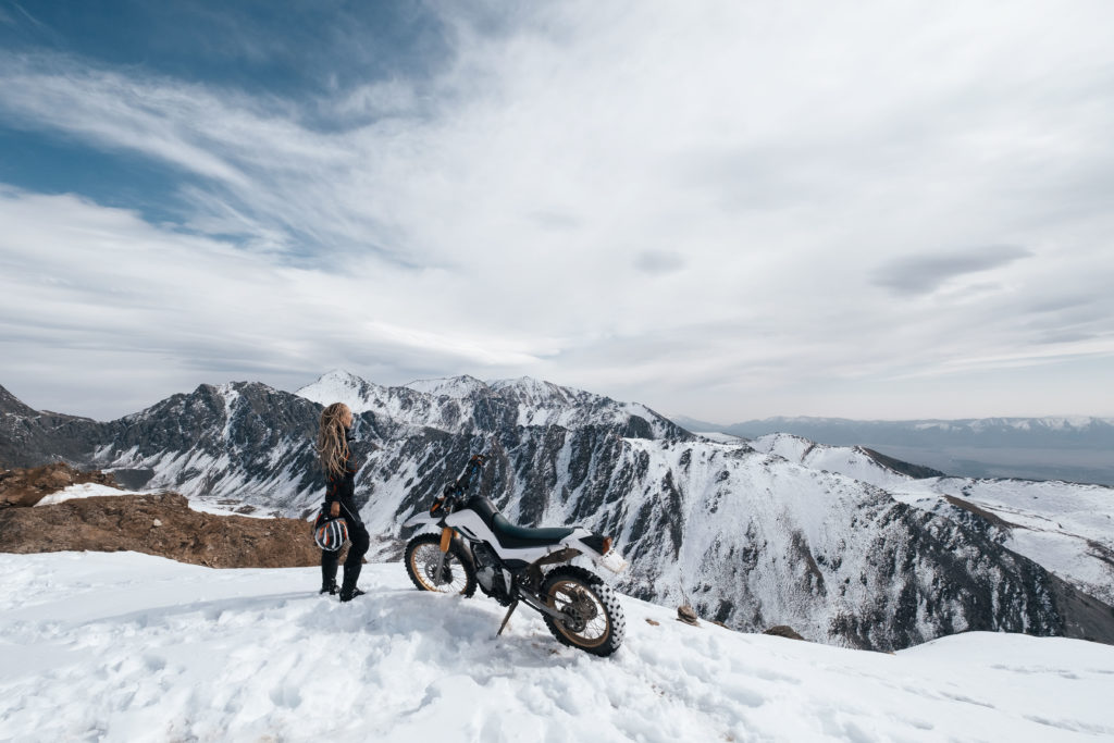 Women in snow next to motorcycle and mountain, Yuasa Battery