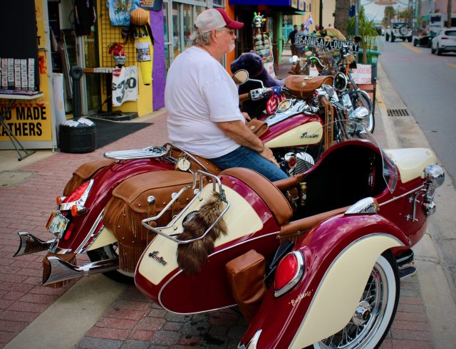 An old biker sits aboard his Indian motorcycle with sidecar along Main Street at Daytona Bike Week 2020.